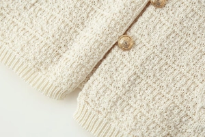 Gros plan du cardigan en maille crème avec boutons métalliques dorés à motifs embossés