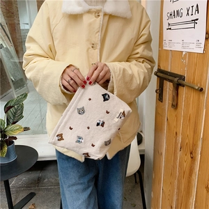 Detailed embroidery of colorful cat faces on a white linen makeup bag held by a person
