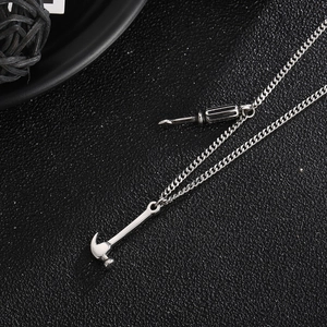 Detail of silver chain necklace with mini hammer and screwdriver tool pendants on black surface