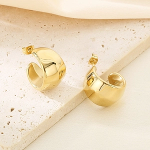 Gros plan de boucles d'oreilles en C plaquées or 18K sur un support en pierre beige neutre