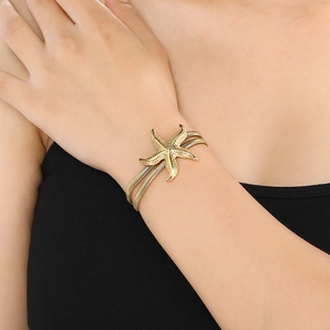 Detail of gold starfish charm bracelet on wrist showing turquoise beads and layered chain