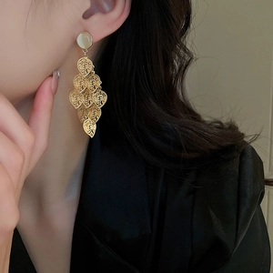 Close-up of long gold fringe earrings with opal stud and leaf design on model