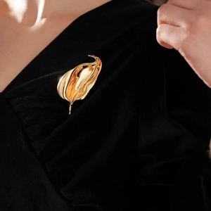 Detailed view of irregular golden leaf brooch pinned on elegant black V-neck clothing