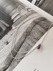 Detail of silver necklace featuring a purple teardrop crystal and a small bird charm