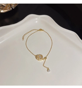 Detail of gold pearl bracelet with zircon flower pendant on decorative white tray
