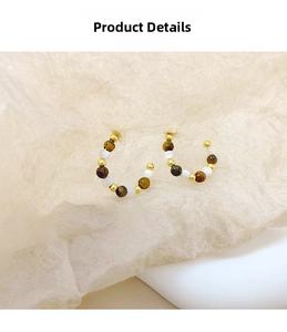 Detail of C-shaped S925 silver stud earrings with tiger eye beads and golden spacers