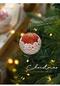 Close-up of a red glitter Christmas ball with white lace hanging on a festive tree