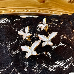 Macro detail of French retro double butterfly earrings in white enamel and gold finish