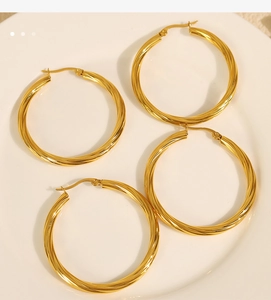 Detail of two pairs of gold twisted hoop earrings placed on a white ceramic dish