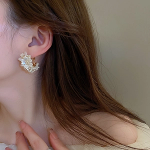 Gold plated flower hoop earrings with pearl luster petals worn by a female model