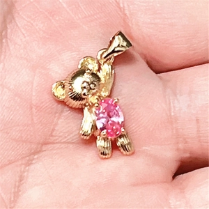 Gros plan d'un pendentif ours doré orné d'un zircon rose tenu dans la main