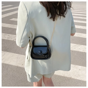 Chic black patent leather mini bag with gold chain strap shown on model outdoors