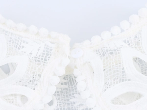 Détail du décolleté en dentelle blanche avec motifs floraux et bordure à pompons