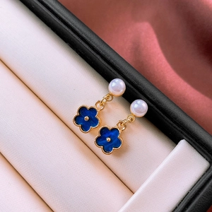 Detail view of gold floral earrings with pearls and blue petals on red satin background