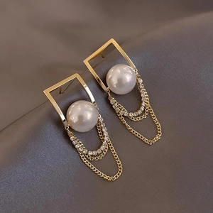 Detail of C-shaped gold earrings with pearls and zircon chains on grey silk fabric