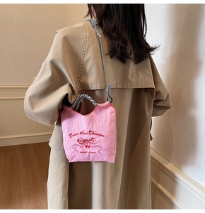 Close-up of pink nylon shoulder bag featuring embroidered cherry patterns and checkered strap