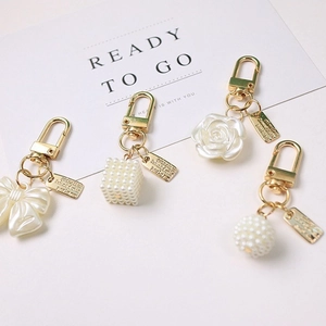 Elegant gold keychain set with rose, bow, and pearl charms on white greeting card background