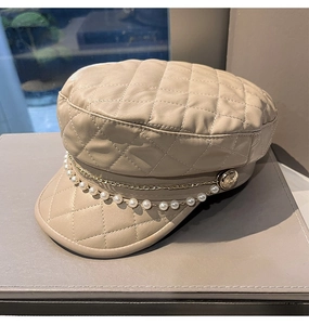 Detailed view of beige quilted leather newsboy cap with pearl and gold metal chains