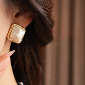 Close-up of vintage square gold stud earrings with pearl inlay worn by a model