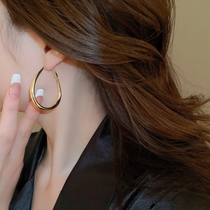 Close-up of model wearing large golden teardrop earrings in polished metal finish