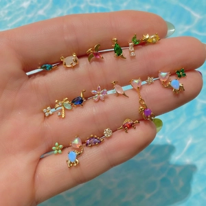 Macro shot of gold animal stud earrings with colorful zircon and opal on hand background