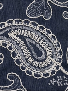 Close-up detail of white paisley embroidery on high-quality navy blue denim fabric