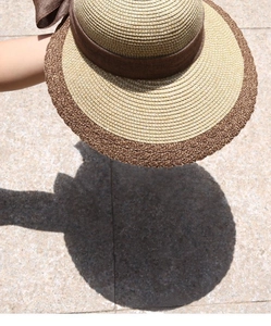 Detail of two-tone beige and brown straw sun hat with satin bow and wavy brim edge