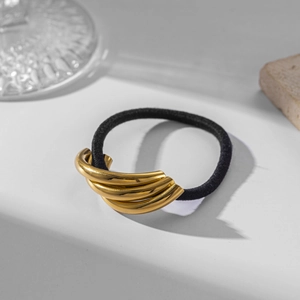 Detail of black elastic hair tie with multilayered golden metal accent on white background