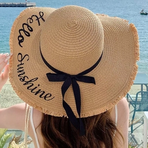 Detail of wide brim straw hat with Hello Sunshine embroidery and black bow decoration