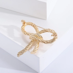 Detail view of a gold bow brooch with woven texture on white geometric steps