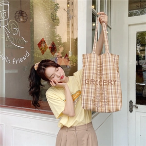 Detail of yellow checkered tote bag featuring a vintage grocery list and brown handles