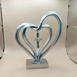 Détail d'une sculpture en forme de cœur argenté avec une croix suspendue sur socle stable