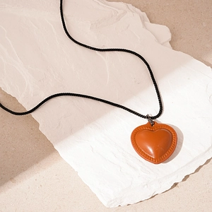 Detailed close-up of an orange heart leather pendant on a black braided rope necklace
