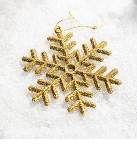 Detail of a sparkling golden snowflake ornament with glitter on white faux snow surface