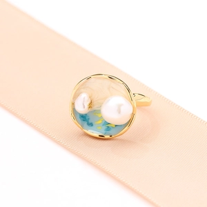 Bague en émail bleu et blanc style vintage avec perles posée sur un ruban rose