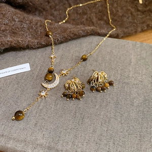 Detail of gold star and moon necklace and fringe earrings set with brown tiger eye stones