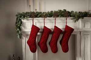 Close-up of four red cable knit Christmas stockings hanging on a white festive fireplace