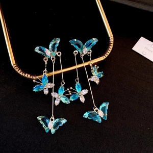 Detailed close-up of long gold chain earrings featuring blue crystal butterflies