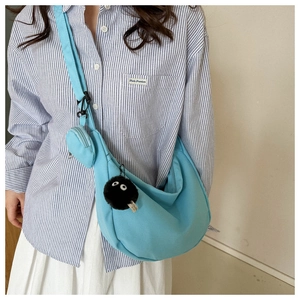 Detail of light blue canvas crossbody bag with a round pouch and black plush charm