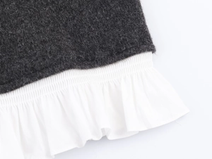 Detailed close-up of dark grey knit fabric stitched with white pleated poplin hemline