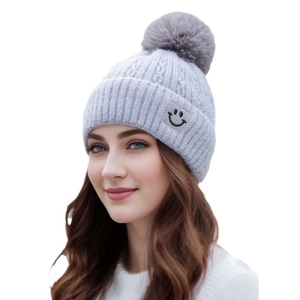 Close-up of gray cable knit beanie featuring a fluffy pompom and a minimalist smile patch