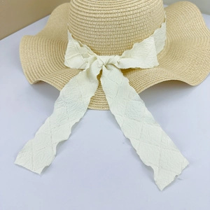 Detail of hand-woven beige straw hat with large brim and elegant white ribbon bow