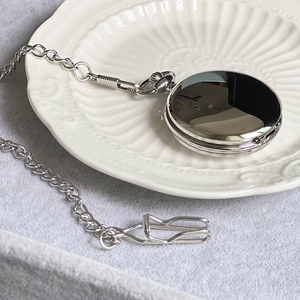Polished silver pocket watch with black dial on a textured white plate and velvet