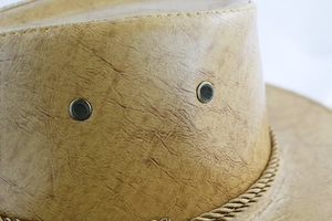 Gros plan d'un chapeau de cowboy en cuir marron avec évents métalliques et bordure tressée