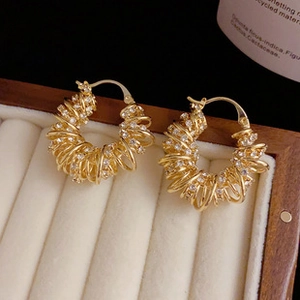 Close-up of golden spiral hoop earrings with pavé white zircons on a beige velvet display