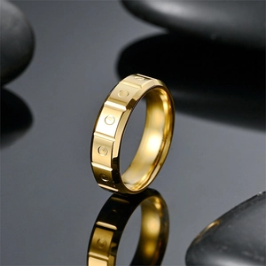 Macro view of gold titanium steel ring with geometric relief pattern on black pebbles