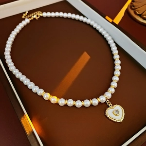 Détail d'un collier de perles plaqué or 18 carats avec pendentif coeur en émail blanc