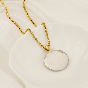 Detail of round two-tone pendant on gold pearl chain displayed on a shell plate