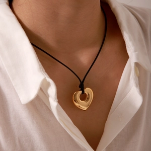 Close-up of a gold heart pendant with a hollow center on a black wax cord for women