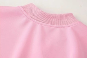 Detailed close-up of pink crew neck ribbing and precision stitching on knit jacket